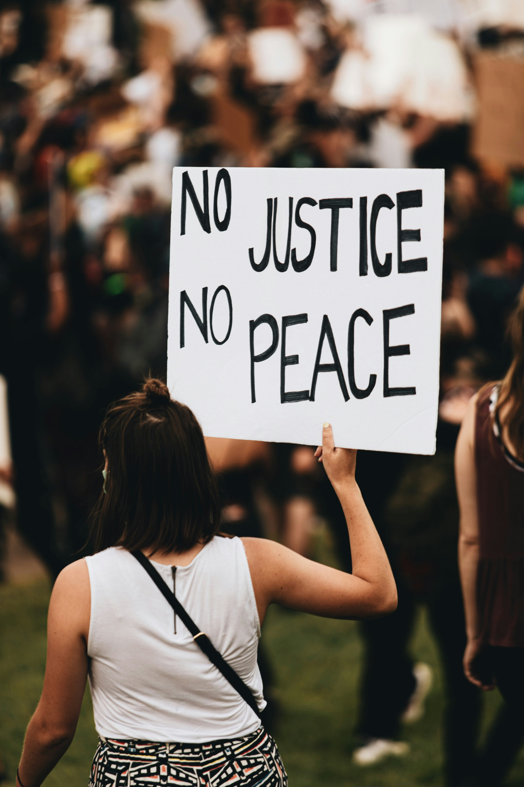 A woman at a rally holding a sign that says, "No Justice No Peace"